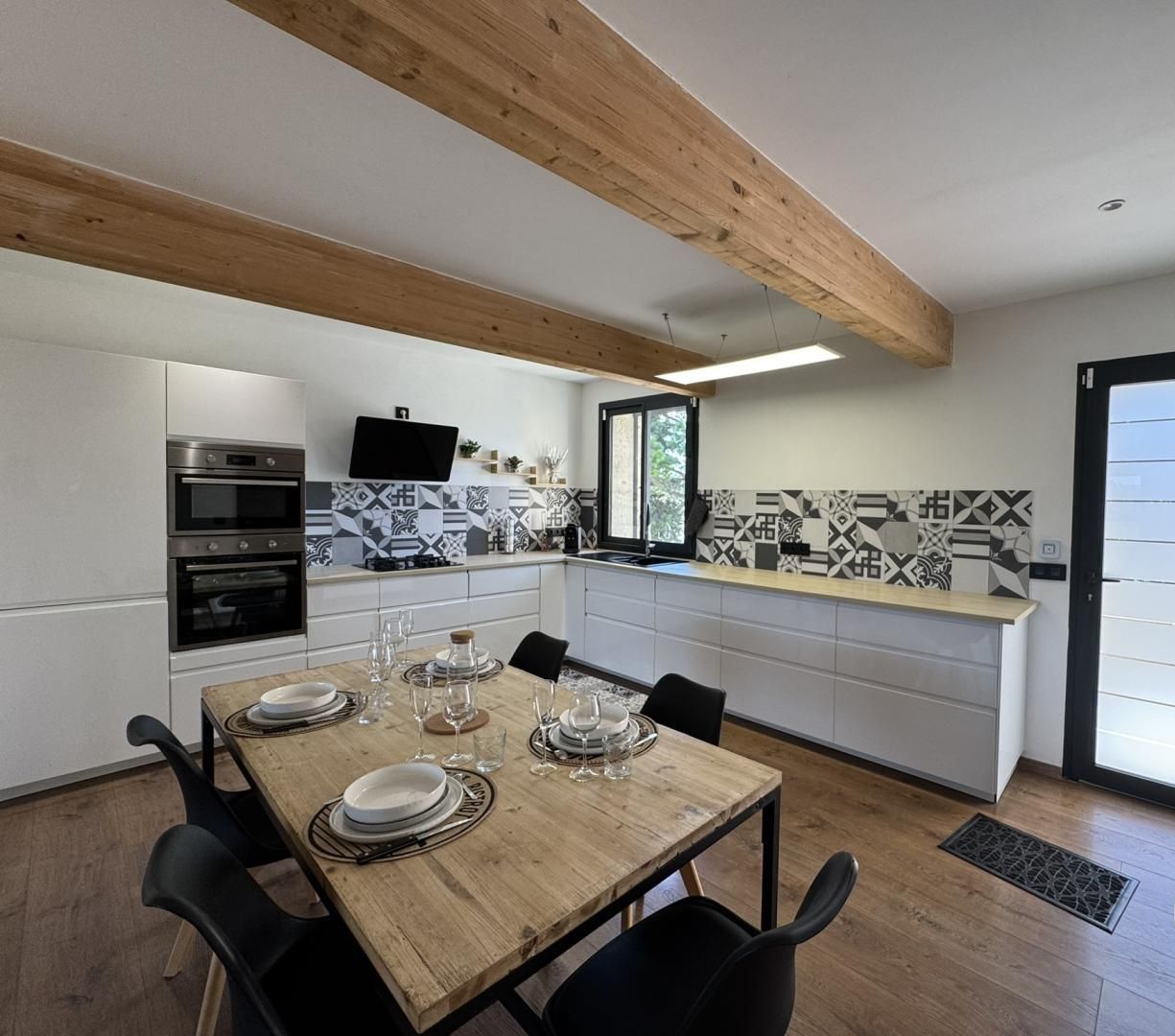 Een moderne keuken met een houten eettafel voor vier personen, witte kastjes en een zwart-wit betegelde achterwand.