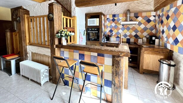 A rustic kitchen with a wooden island, two bar stools, a radiator, and a tiled backsplash.