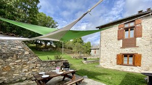 A stone building with wooden shutters, a picnic table set with plates and glasses, and a green canopy.