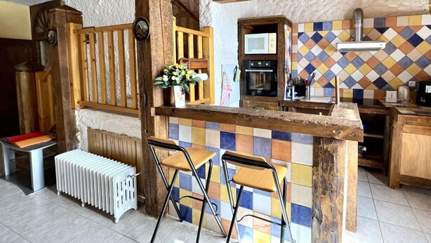 A rustic kitchen with a wooden island, two bar stools, a radiator, and a tiled backsplash. - Bamby's barn - Camurac (Camurac)