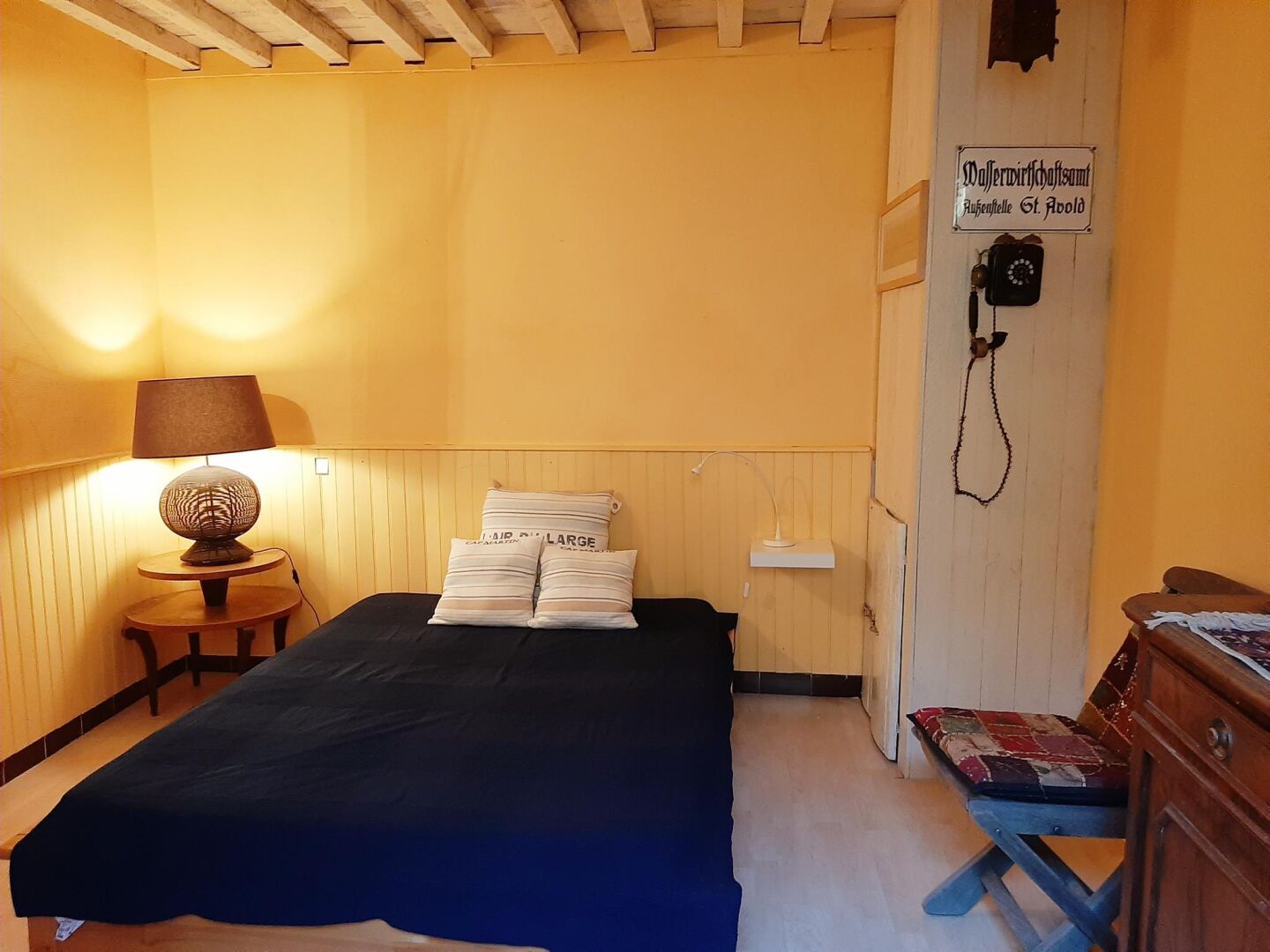 A room with a bed, a desk with a lamp, a chair, and a wooden wall with a sign.