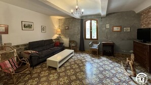 Uma sala de estar com sofá, mesa de centro, cadeiras de vime, televisão e lareira.