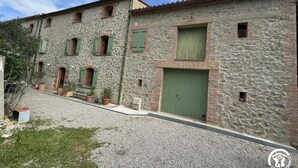 Um edifício de pedra com várias janelas e portas, um caminho de acesso de cascalho e plantas em vasos.