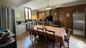 Uma cozinha com mesa de jantar, cadeiras, geladeira, fogão e uma janela.