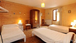 Quarto com duas camas de solteiro, um guarda-roupa de madeira, uma cadeira, um radiador e uma janela com cortinas.