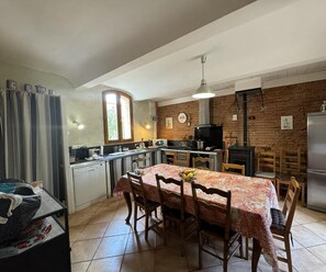 Een keuken met een eettafel, stoelen, een koelkast, een fornuis en een raam.