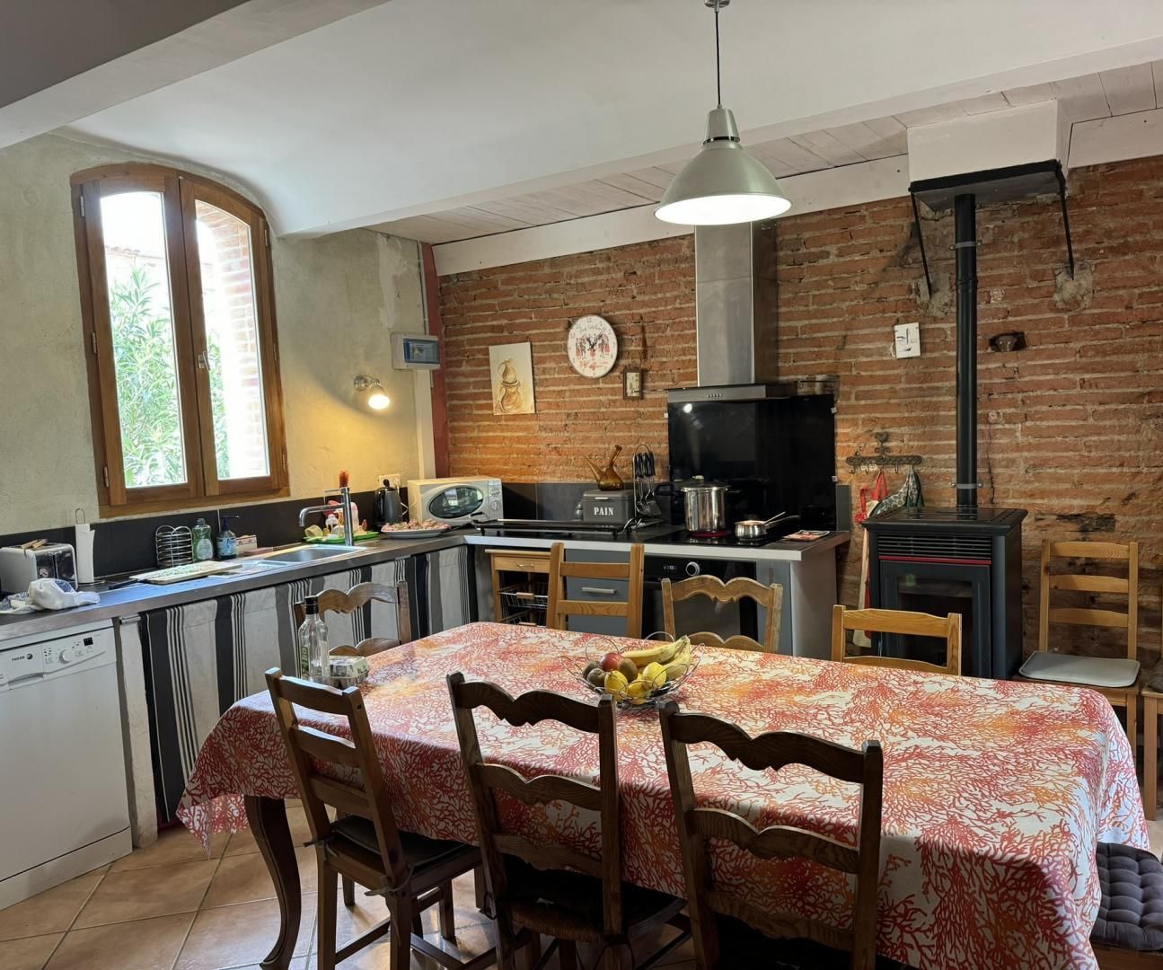 A kitchen with a dining area, featuring a brick wall, a stove, a microwave, and a dining table with chairs.