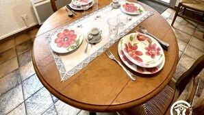 A dining area with a round table set for four, a television on a stand, and a sliding glass door leading to a balcony. - Le Plô du Moulin - VILLENEUVE MINERVOIS (VILLENEUVE MINERVOIS)