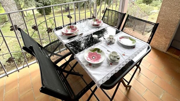 A balcony with a table set for four, surrounded by metal railings, and overlooking a garden with trees and shrubs. - Le Plô du Moulin - VILLENEUVE MINERVOIS (VILLENEUVE MINERVOIS)
