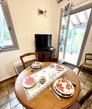 A dining area with a round table set for four, a television on a stand, and a sliding glass door leading to a balcony.
