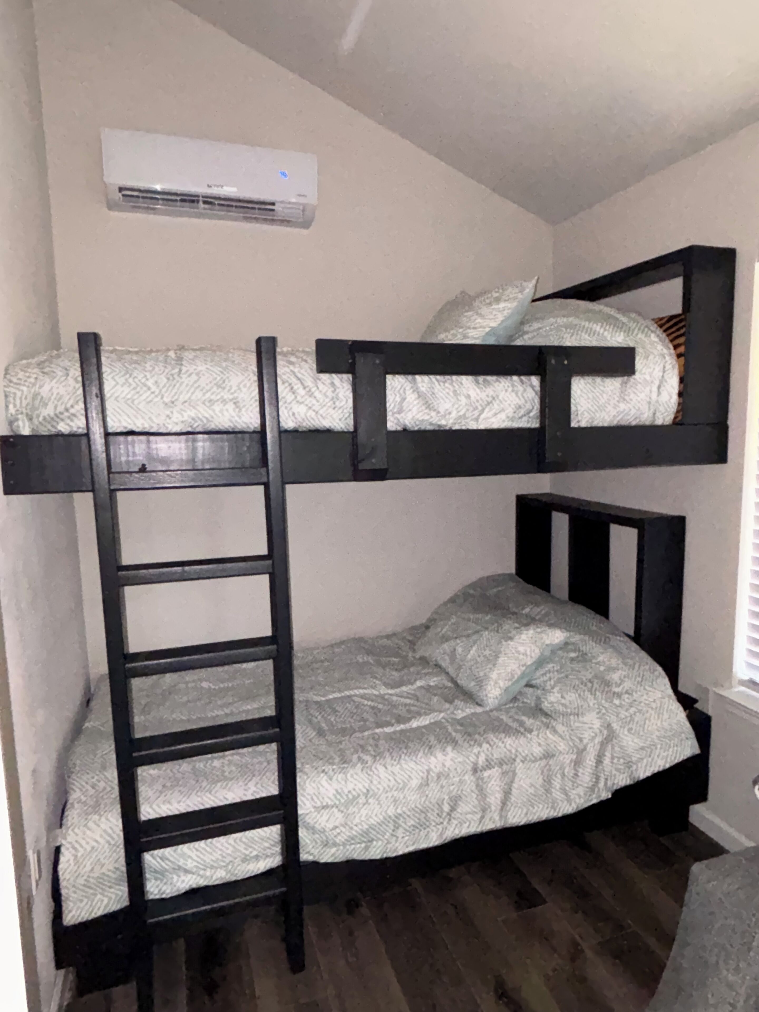 A bunk bed with a ladder, a white air conditioner, and a window with blinds.