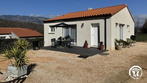 Ein eingeschossiges Haus mit Ziegeldach, einer Terrasse mit Tisch und Stühlen und Kübelpflanzen.