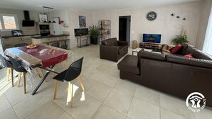 Ein modernes Wohnzimmer mit einem braunen Sofa, einem Esstisch mit Stühlen, einer Küchenzeile und einem Fernseher.