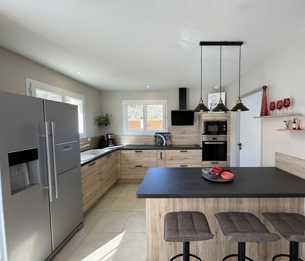 Una cocina moderna con una isla grande, electrodomésticos de acero inoxidable, armarios de madera y encimera negra.