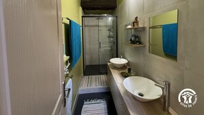 Une petite salle de bain avec une douche, deux lavabos et un miroir.