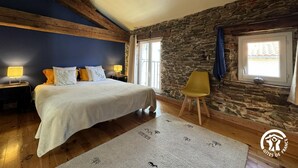 Une chambre à coucher avec un lit, deux tables de chevet avec des lampes, un mur en pierre, une fenêtre et une chaise.