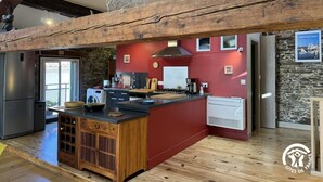 Une cuisine moderne dotée d’un îlot central, de poutres en bois, d’un mur en pierre et d’un mur d’accent rouge.