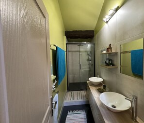 A narrow bathroom with a shower, two sinks, and a mirror.