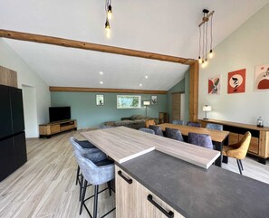 A modern kitchen with a large island, bar stools, and a dining area with a long table. - Gîte du Tatou - ROQUEFEUIL (ROQUEFEUIL)