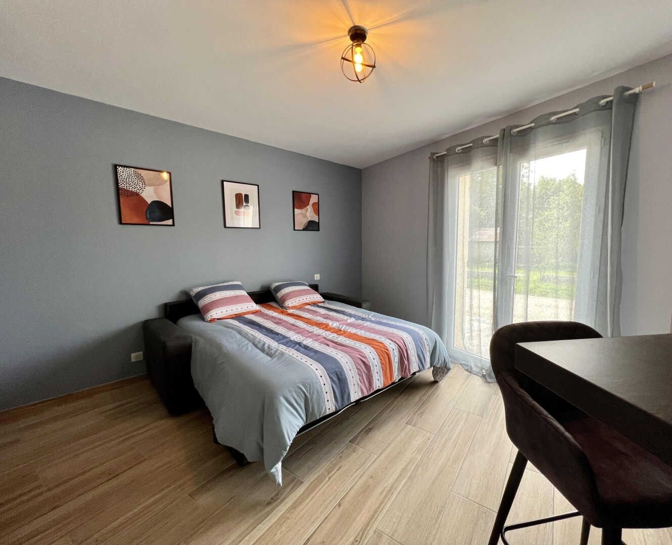 A modern bedroom with a bed, a desk, and a chair. There are three framed pictures on the wall.