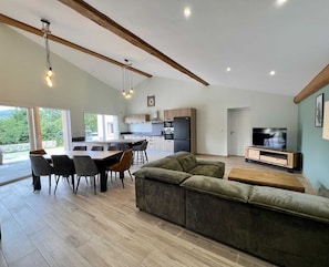 A modern living space with a dining area, kitchen, and a TV in the living room. - Gîte du Tatou - ROQUEFEUIL (ROQUEFEUIL)