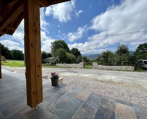 A covered outdoor area with a stone pathway leading to a vehicle, surrounded by greenery and a mountainous backdrop. - Gîte du Tatou - ROQUEFEUIL (ROQUEFEUIL)