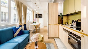Een moderne keuken met houten kastjes, een zithoek met een blauwe bank, en een groot raam met gordijnen.