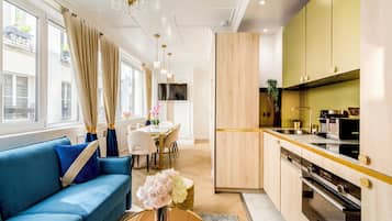 A modern kitchen with wooden cabinets, a dining area with a blue sofa, and a large window with curtains.