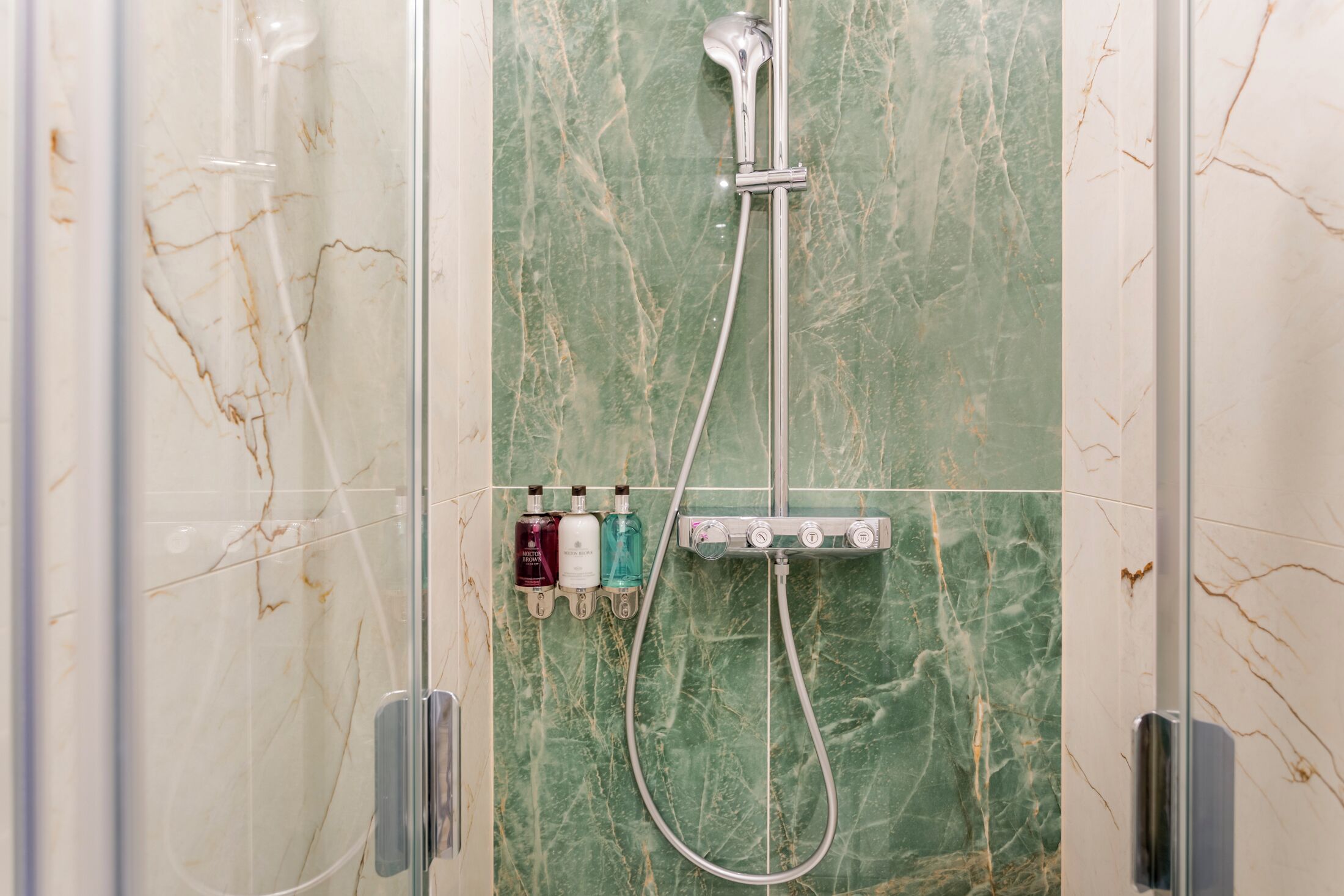 A bathroom with a glass-enclosed shower, a wall-mounted faucet, and three bottles of toiletries.