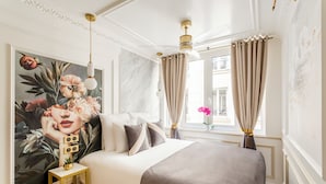 Een smaakvol ingerichte slaapkamer met een groot bed, een decoratieve muurschildering en uitzicht naar buiten door een raam met gordijnen.