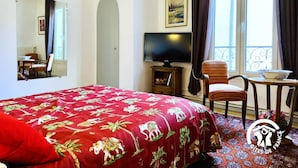 A hotel room with a large bed, a television, a chair, a small table, a window with curtains, and a balcony view. - Saint Genes - CAUNES MINERVOIS (CAUNES MINERVOIS)