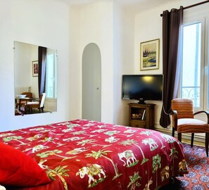 A hotel room with a large bed, a television, a chair, a small table, a window with curtains, and a balcony view. - Saint Genes - CAUNES MINERVOIS (CAUNES MINERVOIS)