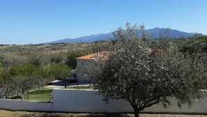 A rural landscape with a house, a tree, and mountains in the background.
