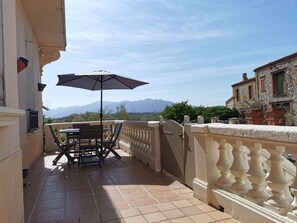 Ein Balkon mit Tisch, Stühlen, einem Sonnenschirm und Blick auf Berge.