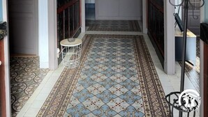 A hallway with patterned floor tiles, a decorative ceiling, and a door leading to a room with a tiled floor.