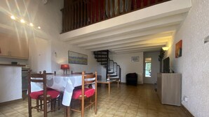 A spacious living area with a dining table, chairs, a staircase, and a television. - Le yucca - ALENYA - Gîte (ALENYA)