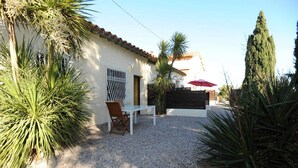A patio with a white table and chairs, surrounded by palm trees and a gravel ground. - Le yucca - ALENYA - Gîte (ALENYA)
