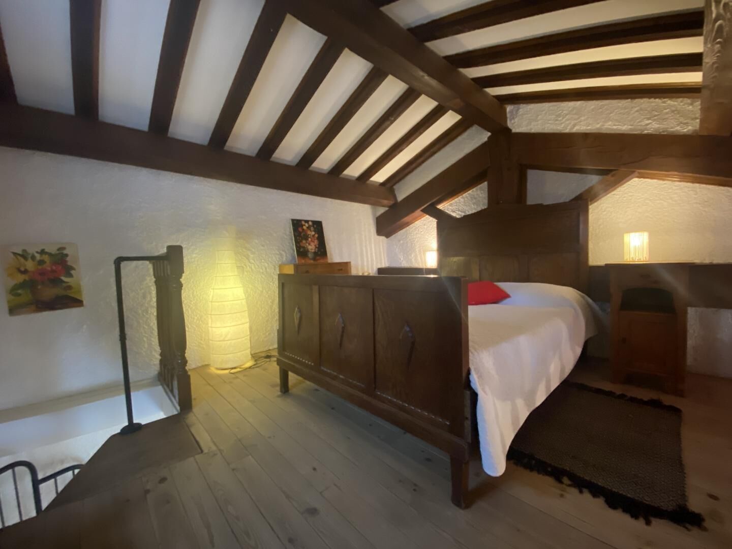 Een slaapkamer met een houten bed, een nachtkastje, een wandlamp en een schilderij.