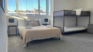 A bedroom with a bunk bed, a single bed, a lamp, and a view of the city through large windows.