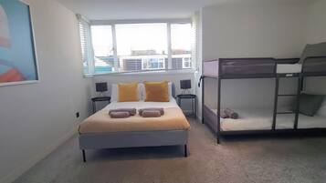 Une chambre à coucher comprenant un lit, un lit superposé, deux tables de chevet et une fenêtre avec des stores.