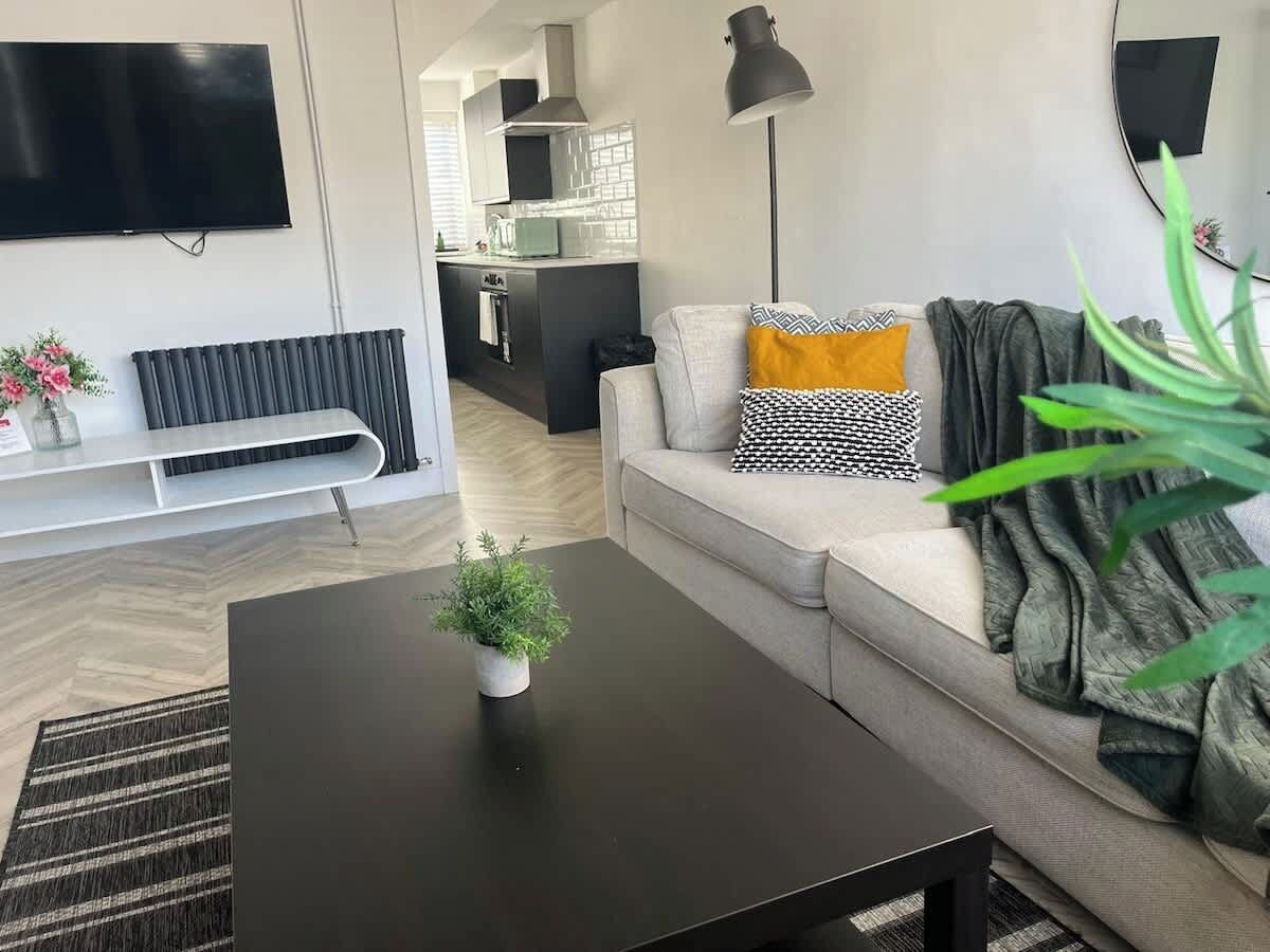 A modern living room with a black coffee table, a sofa with patterned cushions, a potted plant, and a television mounted on the wall.