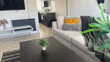 A modern living room with a black coffee table, a sofa with patterned cushions, a potted plant, and a television mounted on the wall.