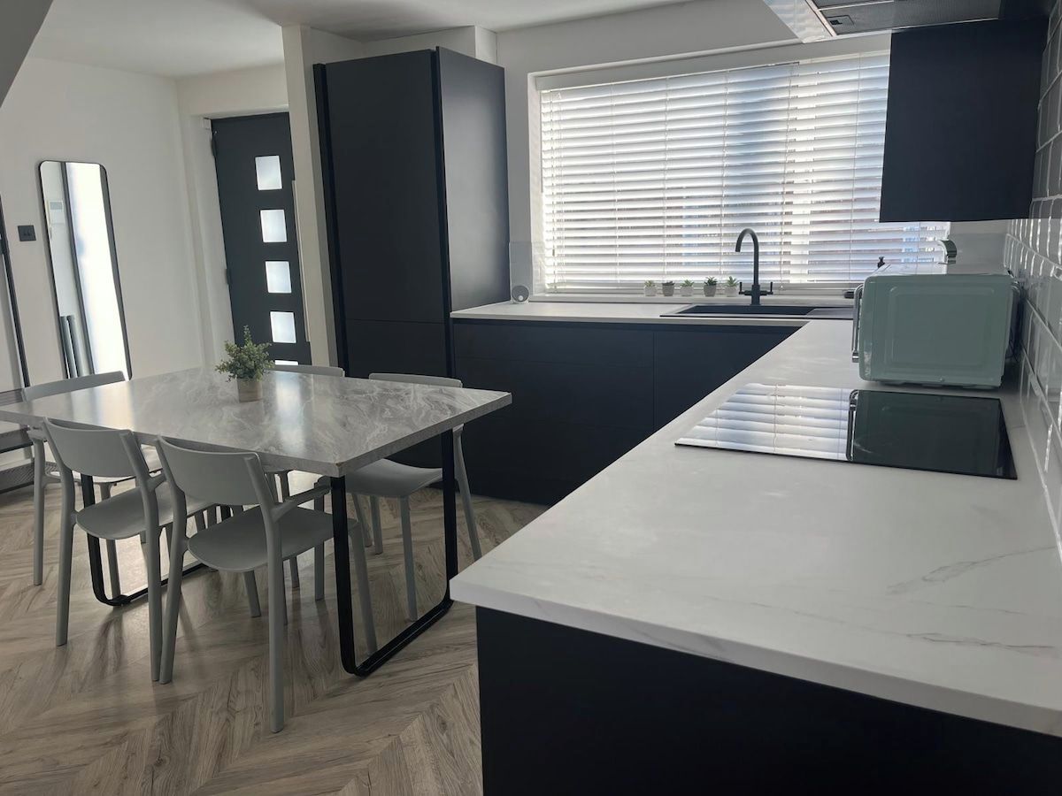 A modern kitchen with a marble countertop, a dining table with chairs, a black cabinet, and a window with blinds.