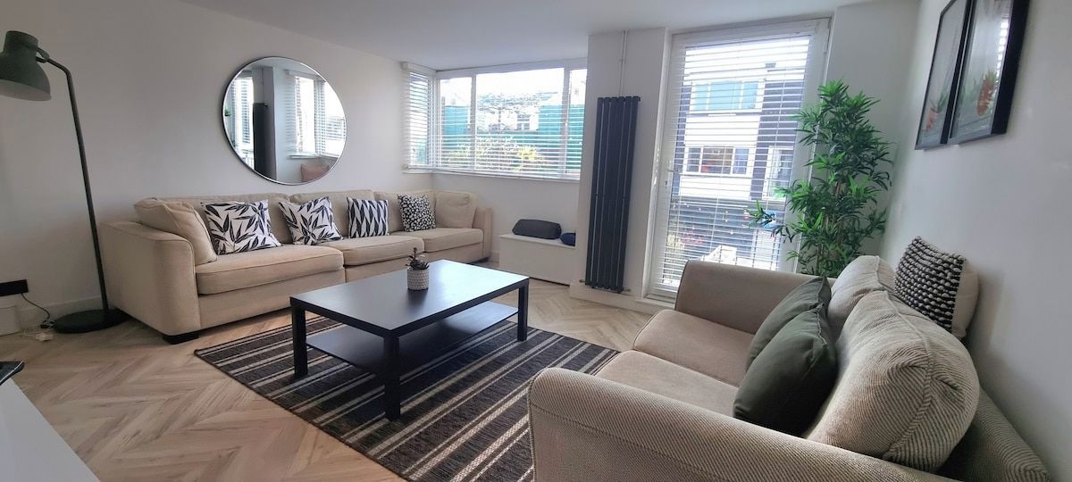 Ein modernes Wohnzimmer mit einer Couch, einem Couchtisch und einem großen Fenster mit Jalousien.