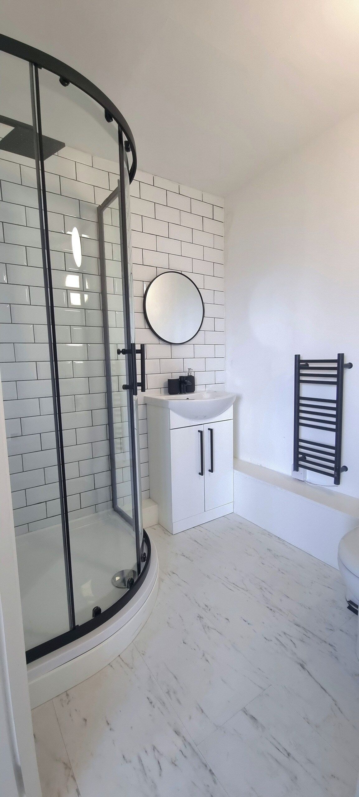Un bagno con box doccia in vetro, lavandino bianco con specchio soprastante e porta asciugamani nero.