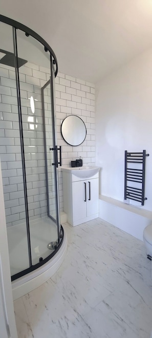 Un bagno con box doccia in vetro, lavandino bianco con specchio soprastante e porta asciugamani nero.