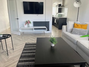 A modern living room with a black coffee table, a grey sofa with patterned cushions, a flat-screen TV mounted on the wall, and a small plant on the table. - Brighton Lanes Stay – Parking & Shared Patio (Brighton and Hove)