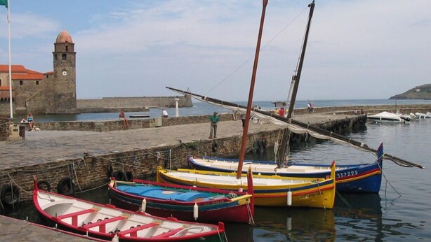 A harbor with several colorful boats docked, a stone tower, and a calm sea.