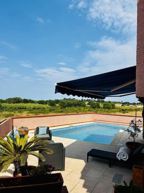 A swimming pool with lounge chairs and a covered area, surrounded by greenery and a clear sky. - Studio MOZ'ART - BAGES (BAGES)