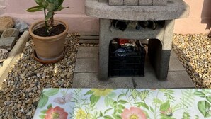 A concrete barbecue grill with a metal grate, a potted plant, and a table with a floral tablecloth.